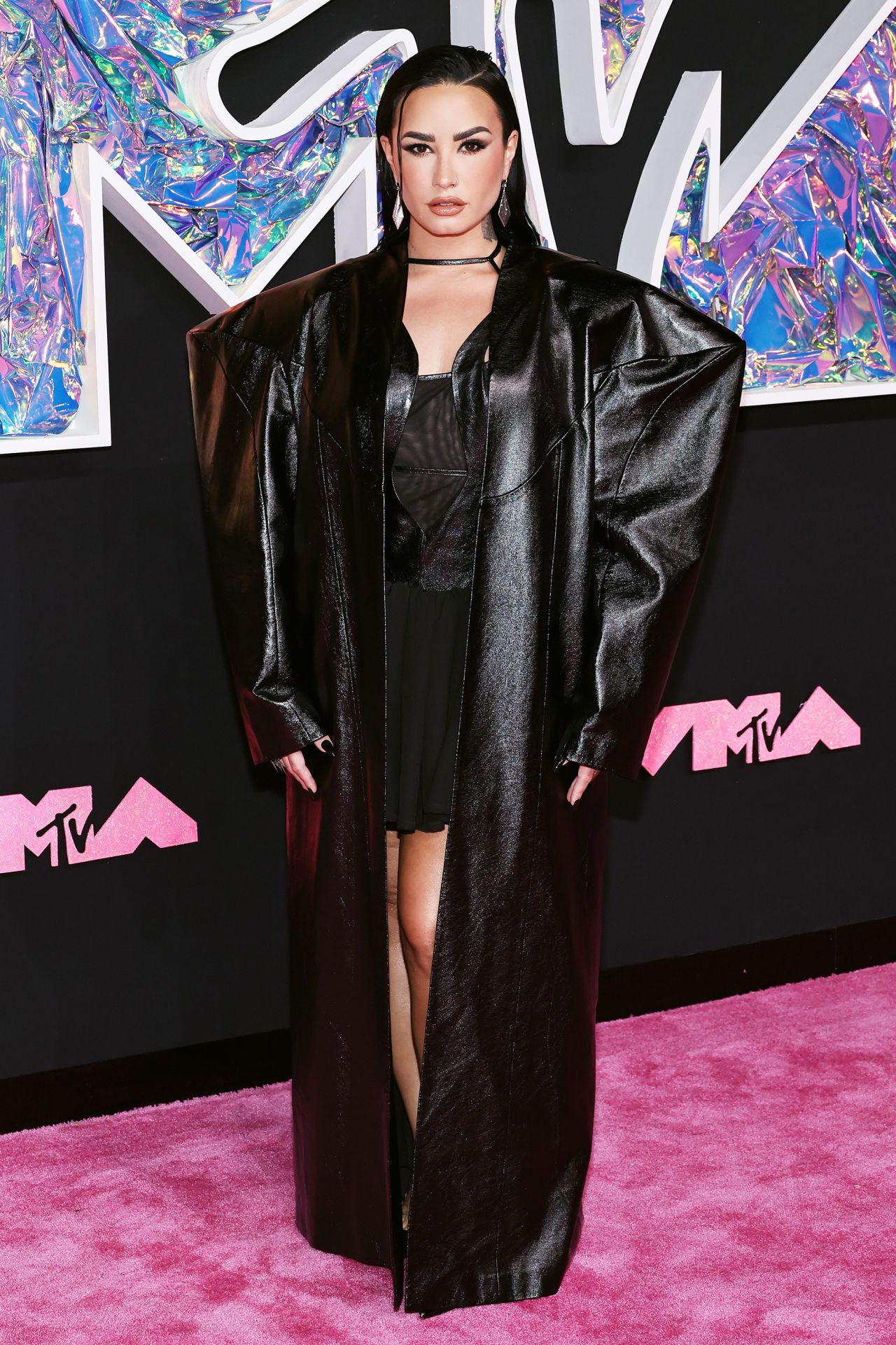 Demi Lovato looked edgy in an oversized geometric black coat layered with a mesh and leather mini dress resembling the one she wore on the cover of her forthcoming album