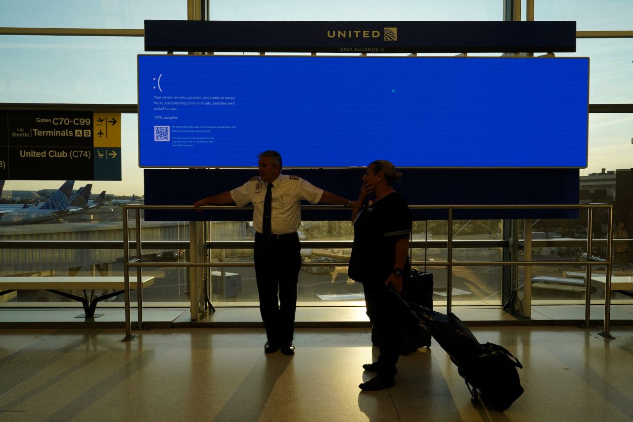 United Airlines employees wait by a departures monitor displaying a blue error screen, also known as the "Blue Screen of Death" at Newark International Airport in New Jersey.