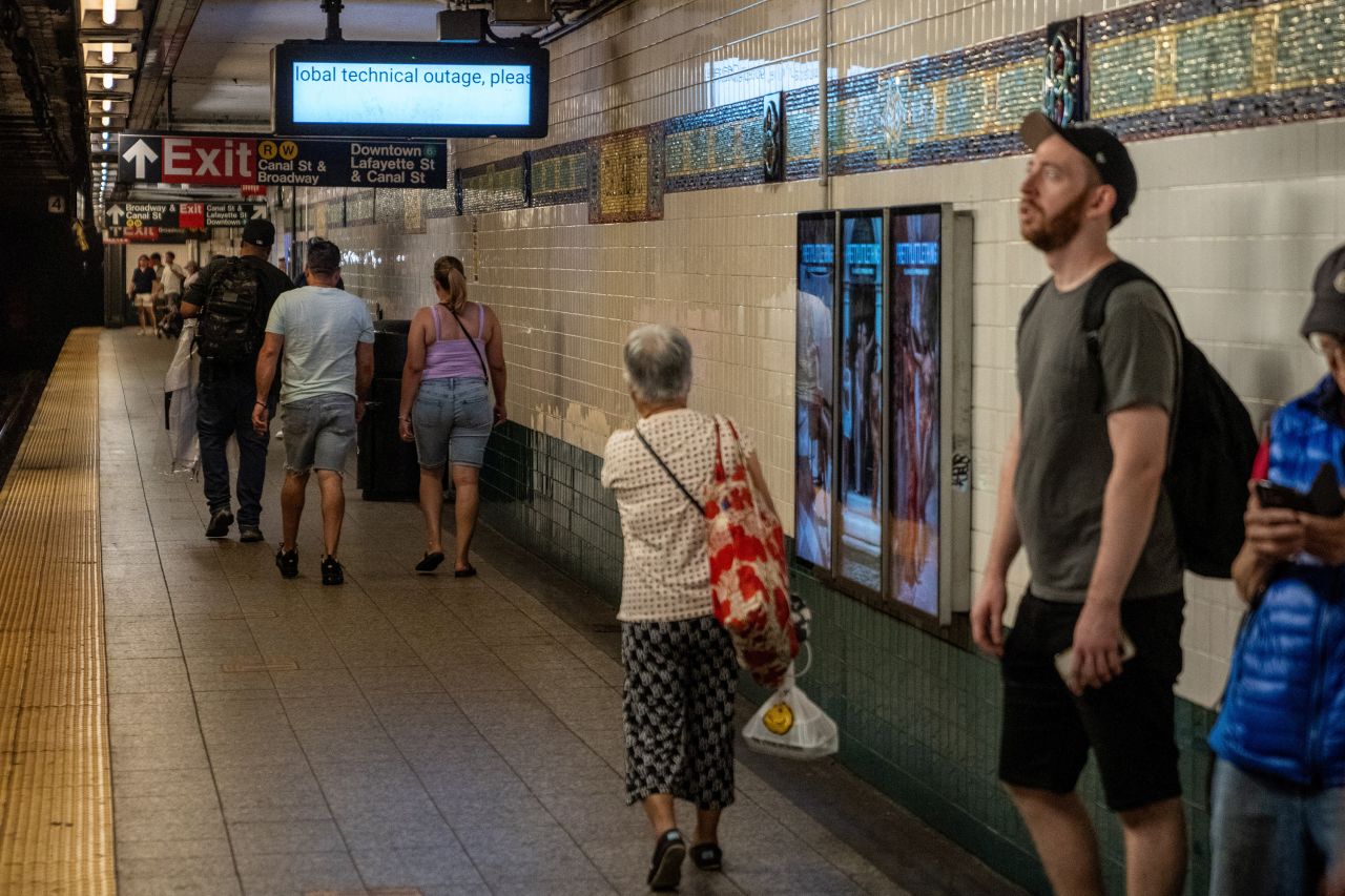 People walk by a digital sign, which normally displays train times, as it shows information about a technology outage in New York on July 19.