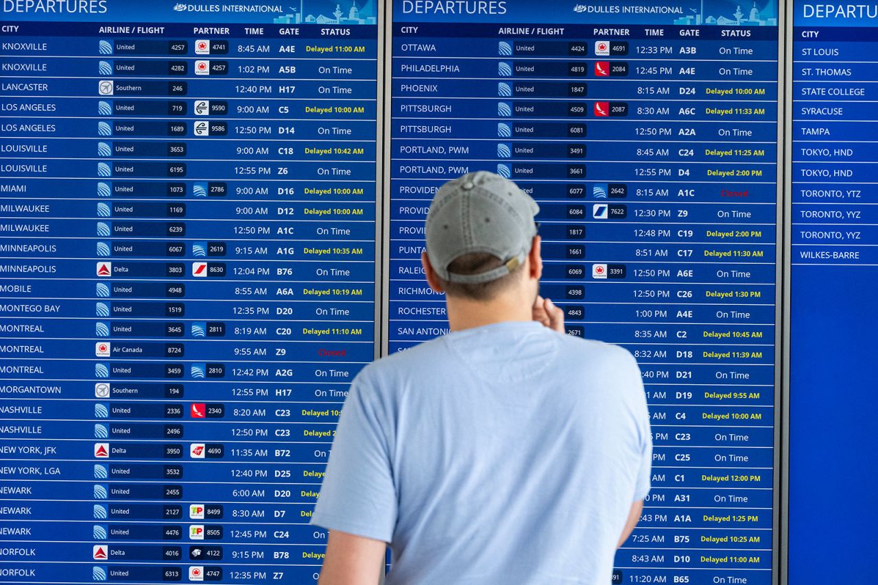 A passenger looks at a flight information board showing multiple delays and some cancellations in flight departures from Dulles International Airport on Friday, July 19, in Dulles, Virginia. 