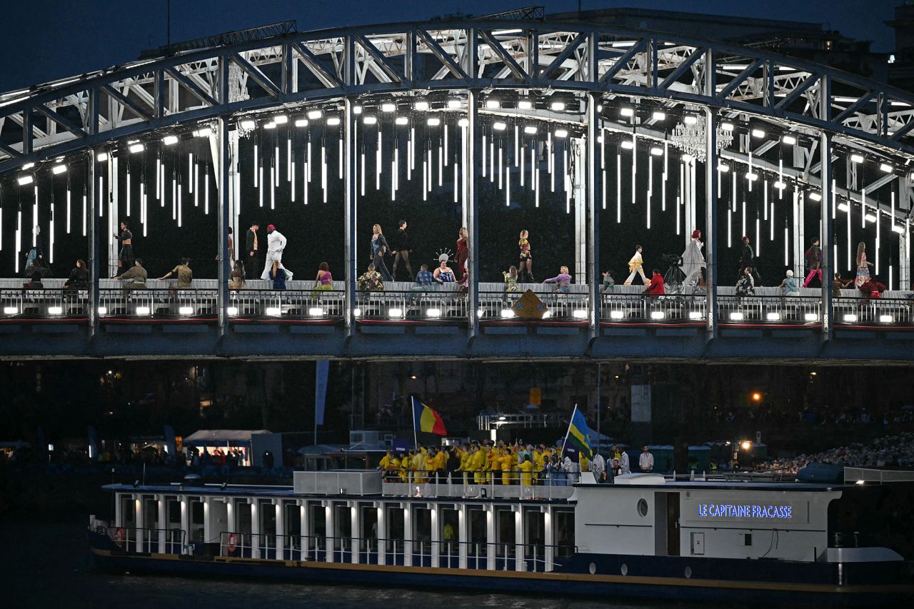 Models present creations while walking a catwalk erected along the Passerelle Debilly bridge as the boat carrying the delegations of Romania and Rwanda sails underneath along the Seine river.