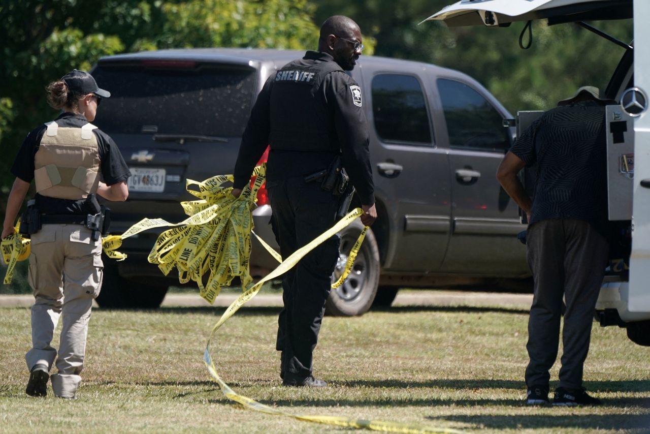 Law enforcement officers hold police tape near the scene.