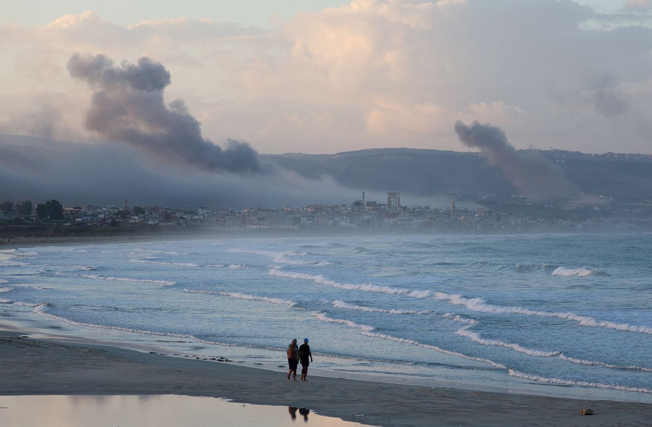 People walk at a beach as smoke billows over southern Lebanon following Israeli strikes, as seen from Tyre, southern Lebanon September 23. 