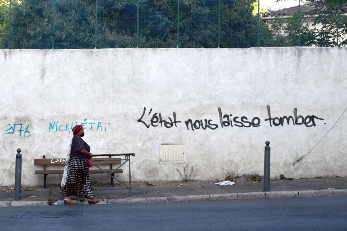 A woman walks past graffiti on a wall reading "State lets us down" in a street in Les Marronniers neighborhood in Marseille in August 2021.