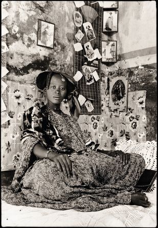 “Portrait of Mrs. Fatou Thioune, Saint Louis,” by Macky Kane, c.1939–1941. This photograph shows Thioune posing in front of her “xoymet,” a Wolof word for a photographic collage associated with brides in the lead up to their wedding. Images were collected from friends and family and arranged by a specialist, with<strong> </strong>the xoymet visited by the bride’s social circle in the lead up to the big day. The uniquely Senegalese social practice sprung up in the 1930s and died out in the 1960s, for reasons unknown, said Paoletti.