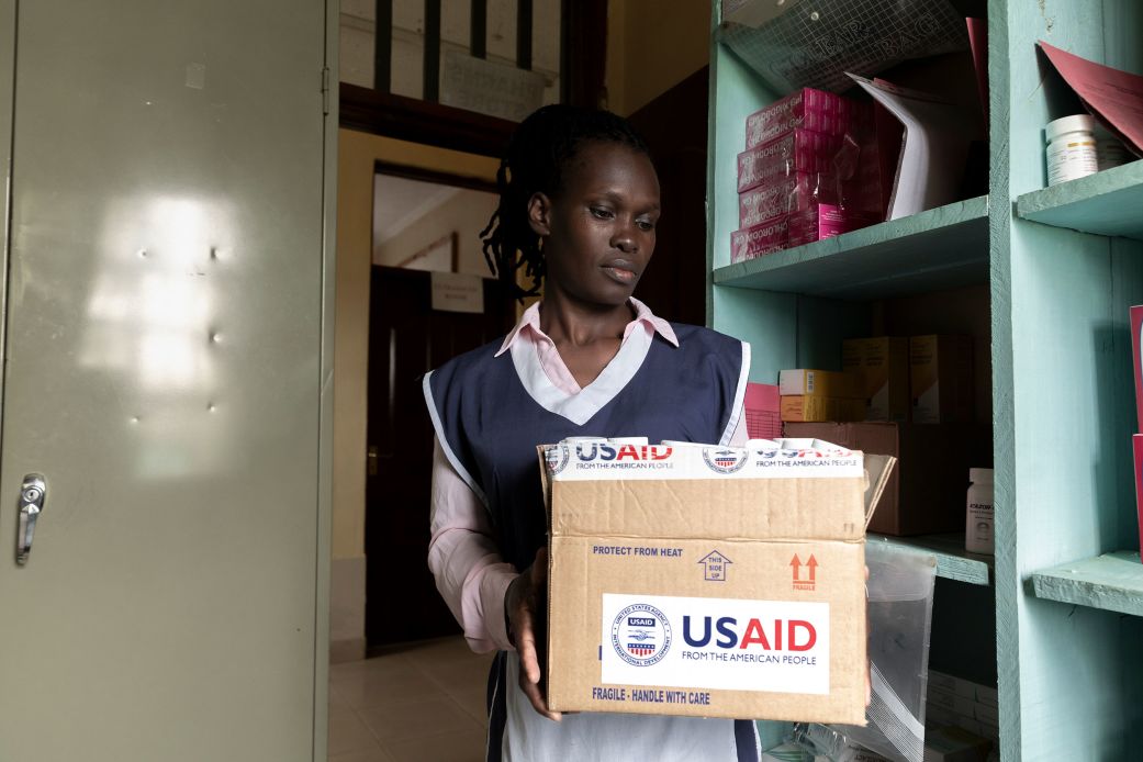 In a stockroom of Kuoyo Sub-county Hospital in Kisumu, Kenya, a nurse holds a USAID-labeled box containing antiretroviral medicine in April, as US funding cuts ripple through the health system.
