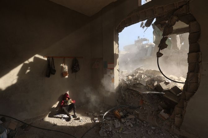 A Palestinian boy holds a book Tuesday, April 29, as he sits in the rubble of a house following Israeli strikes at the Nuseirat refugee camp in central Gaza.
