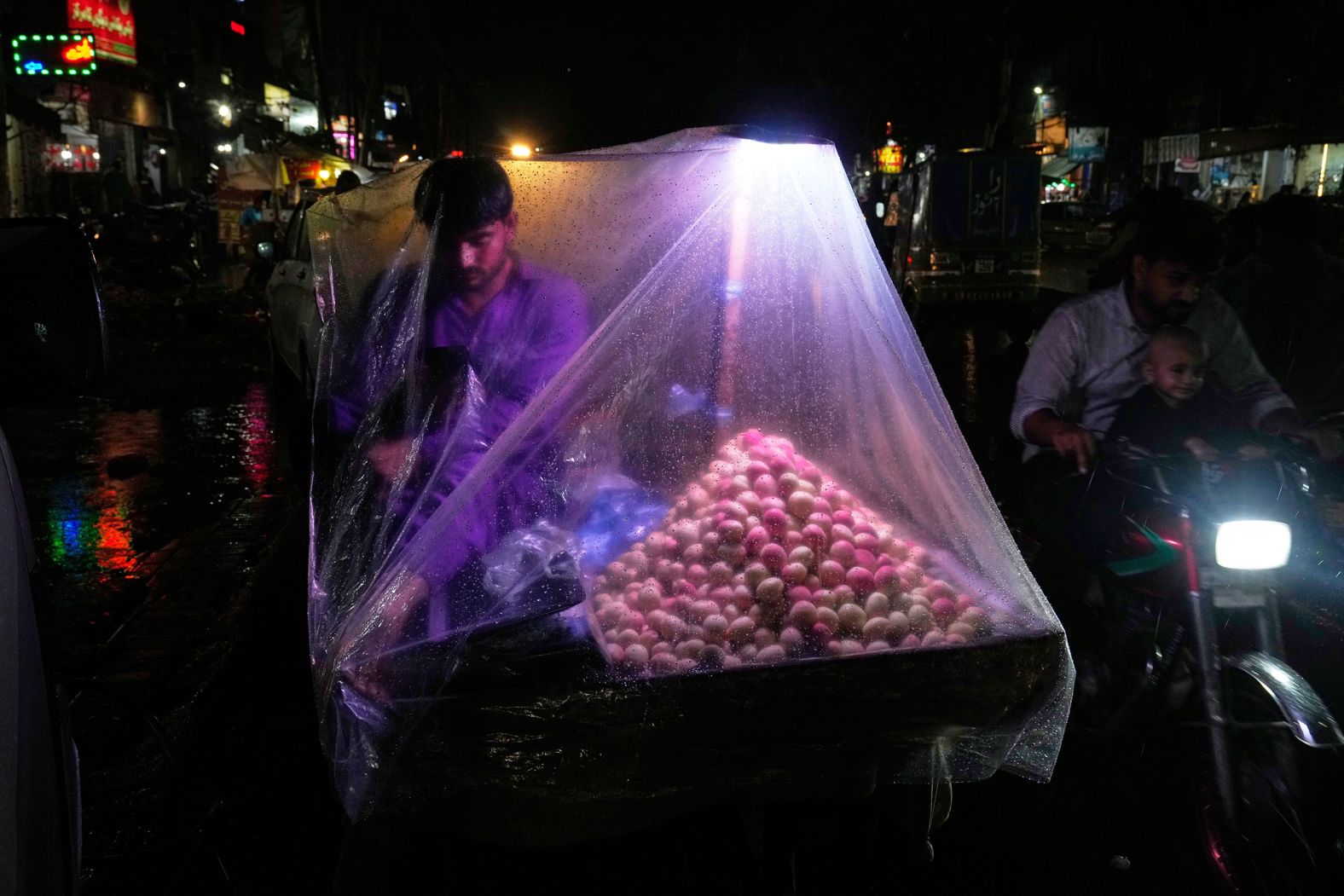 A street vendor protects himself and his goods with a plastic sheet during a rain storm in Lahore, Pakistan, on July 15.
