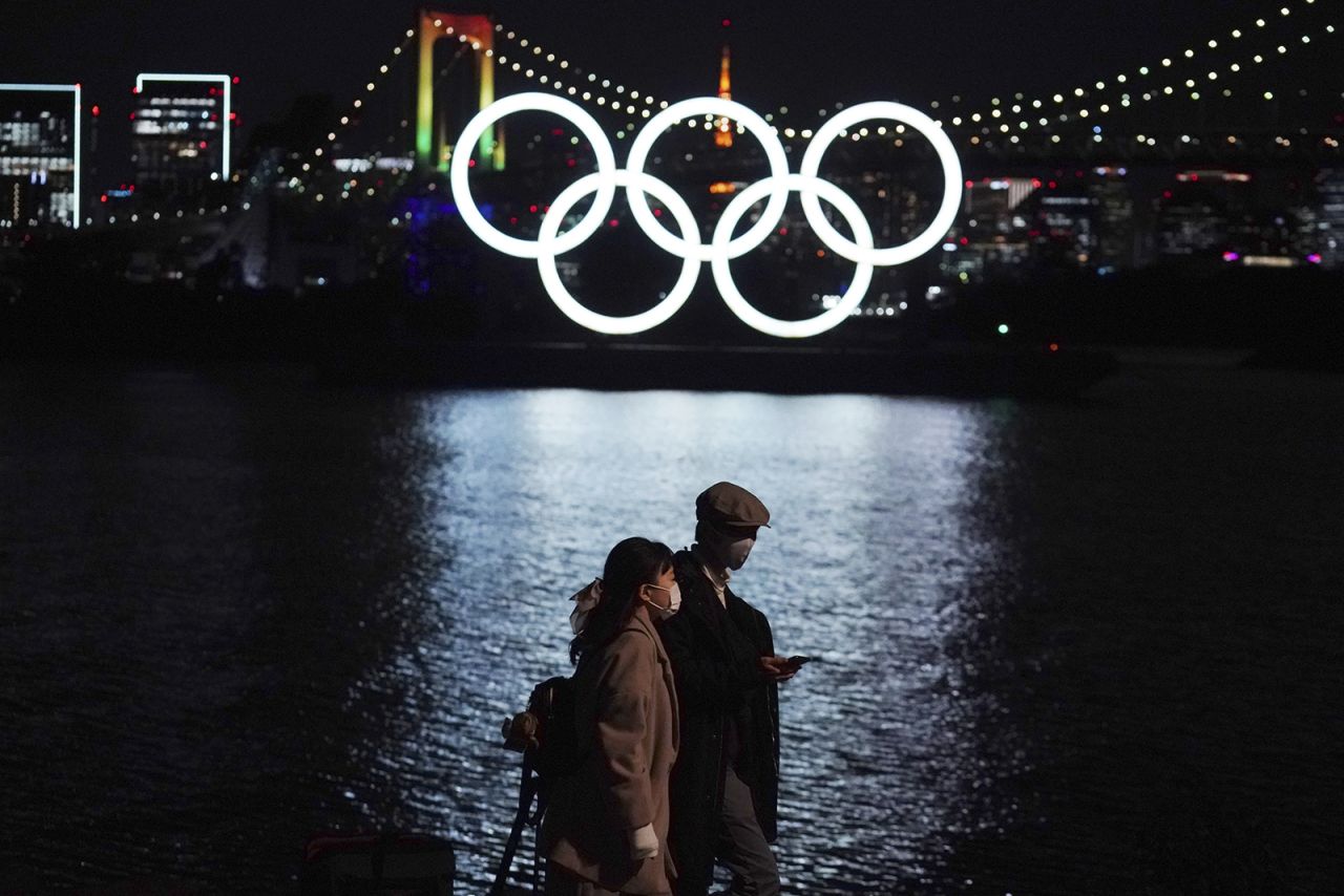 A man and a woman walk near the Olympic rings floating in the water on Dec. 1 in the Odaiba area of Tokyo.