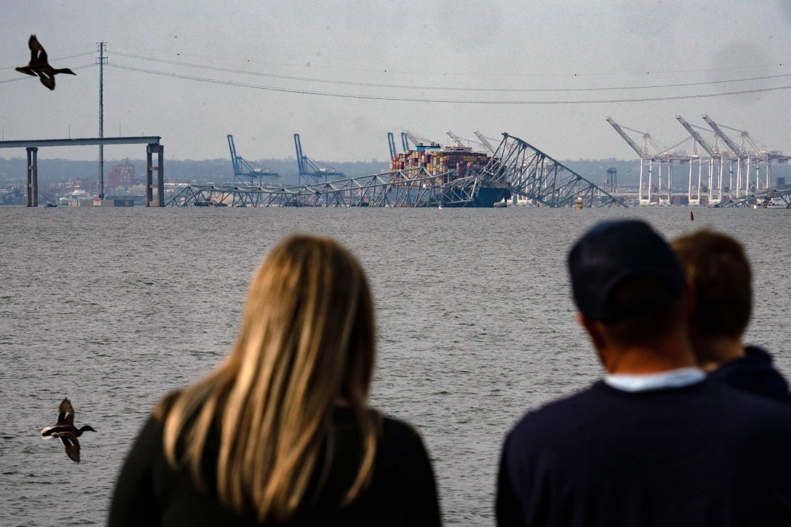 A family looks at the steel frame of the Key Bridge sitting on top of the container ship.