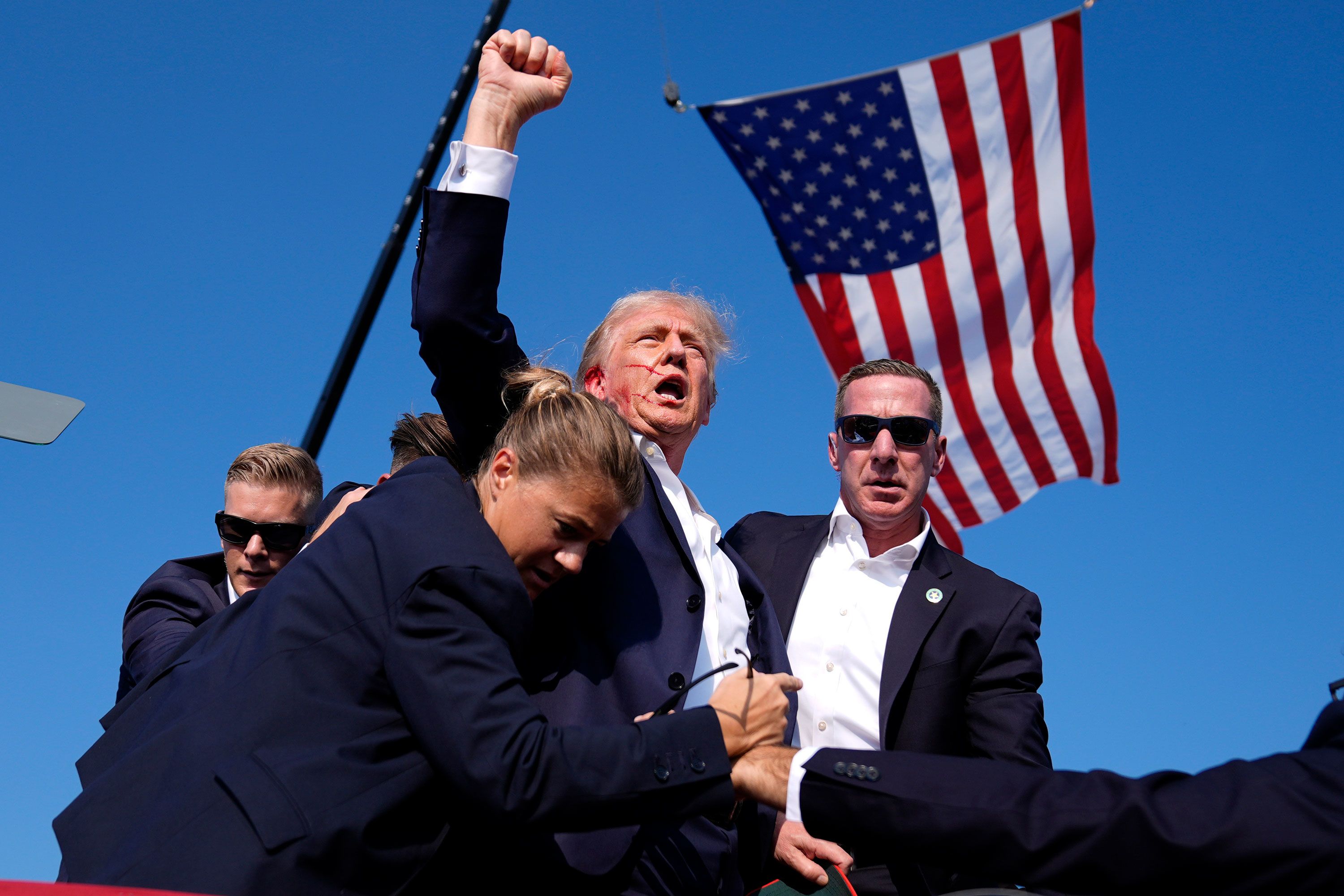 Former US President Donald Trump, with blood on his face, raises his fist to the crowd as he is helped by Secret Service agents at his campaign rally in Butler, Pennsylvania, on Saturday, July 13. Trump’s right ear was struck by a bullet during an assassination attempt.