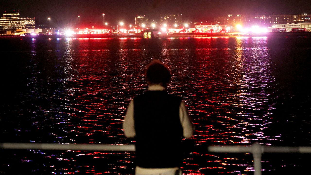 A person looks on from the bank of the Potomac River as emergency service vehicles operate near the site of the crash after American Eagle flight 5342 collided with a helicopter while approaching Ronald Reagan Washington National Airport and crashed in the Potomac River, outside Washington, U.S., January 29, 2025. REUTERS/Carlos Barria   