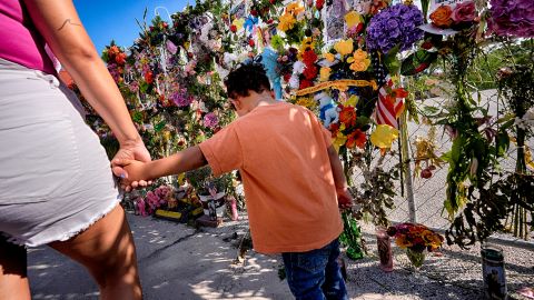 Danielle Alonzo walks with her son Krew at a memorial wall of flowers and photos for flood victims prior to a vigil on Friday, July 11, 2025, in Kerrville, Texas. (AP Photo/Gerald Herbert)