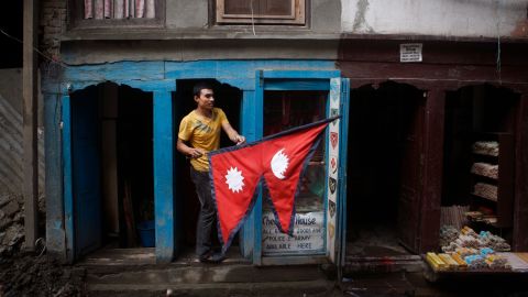 A man carries a Nepali flag as he stands outside his stall in Kathmandu, (AP Photo/Niranjan Shrestha)