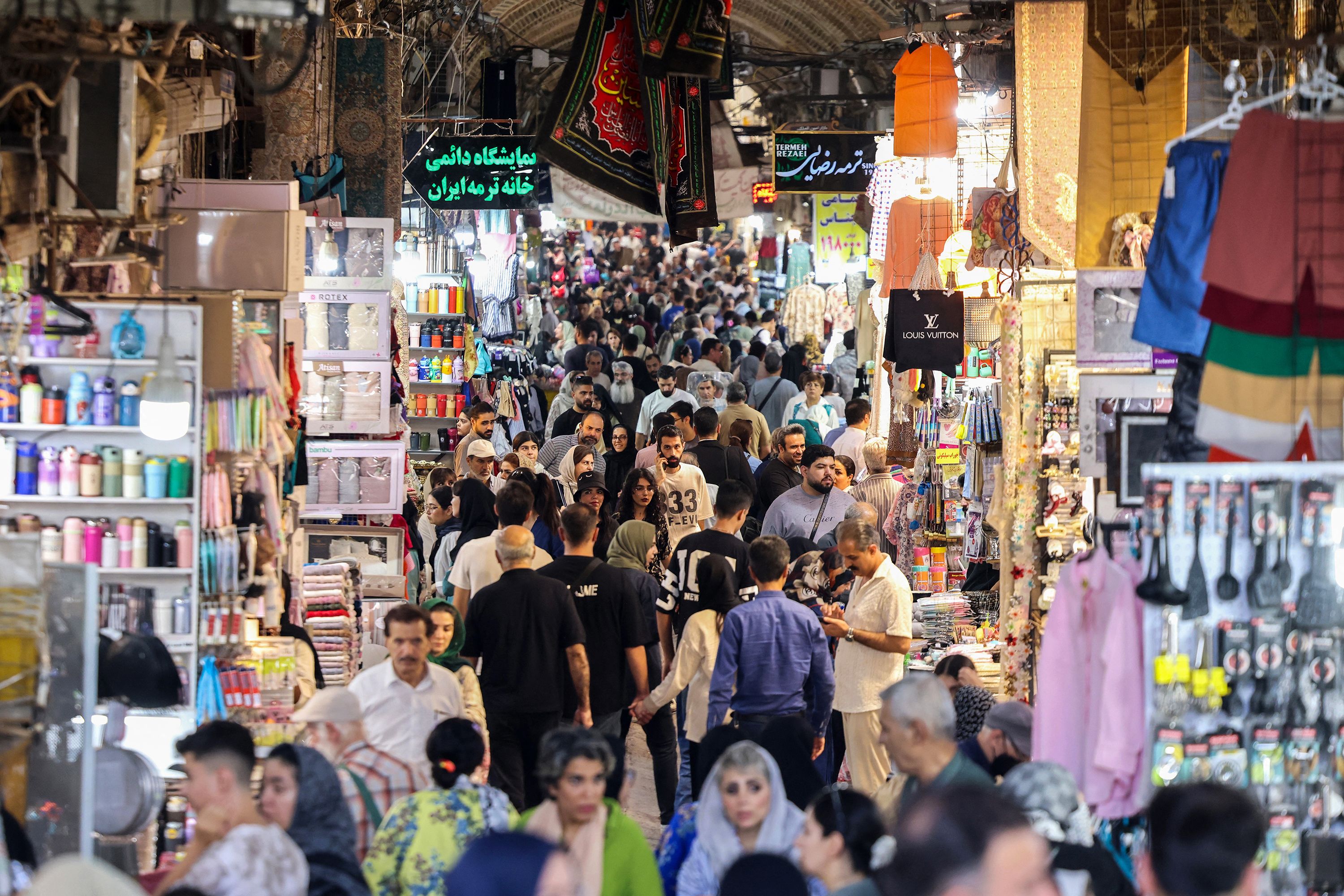 ایرانیان در ۱۳ آگوست از کنار مغازه‌های بازار بزرگ تهران عبور می‌کنند. بر اساس آمار اکتبر صندوق بین‌المللی پول، قیمت کالاهای اساسی در ایران افزایش یافته و نرخ تورم سالانه به ۴۲.۴% رسیده است. عطا کناره/خبرگزاری فرانسه/گتی ایمیجز
