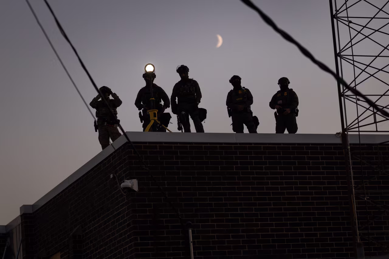 Federal law enforcement agents watch demonstrators outside of an immigrant processing center in Broadview, Illinois on September 27.