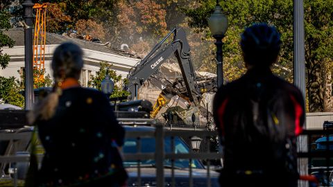 Pedestrians stop and watch the facade of the East Wing of the White House being demolished on Tuesday.