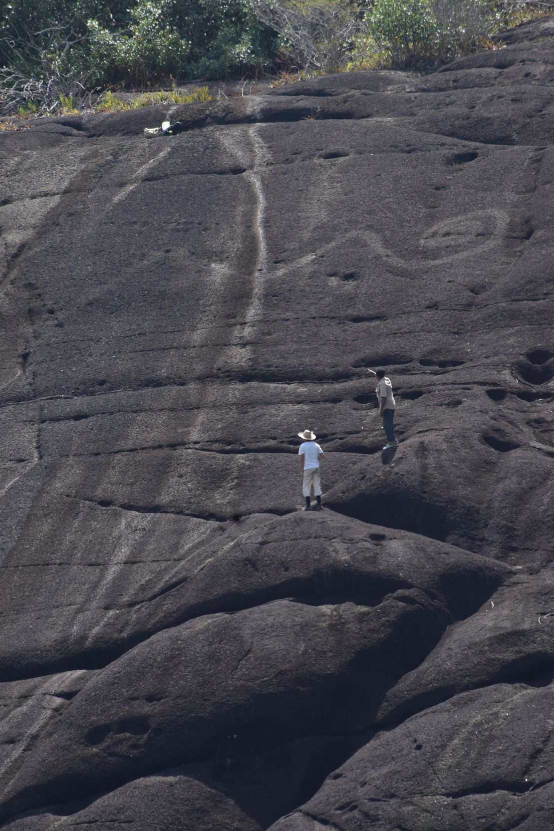 Monumental rock art of a snake tail in Colombia dwarfs the humans in this image.