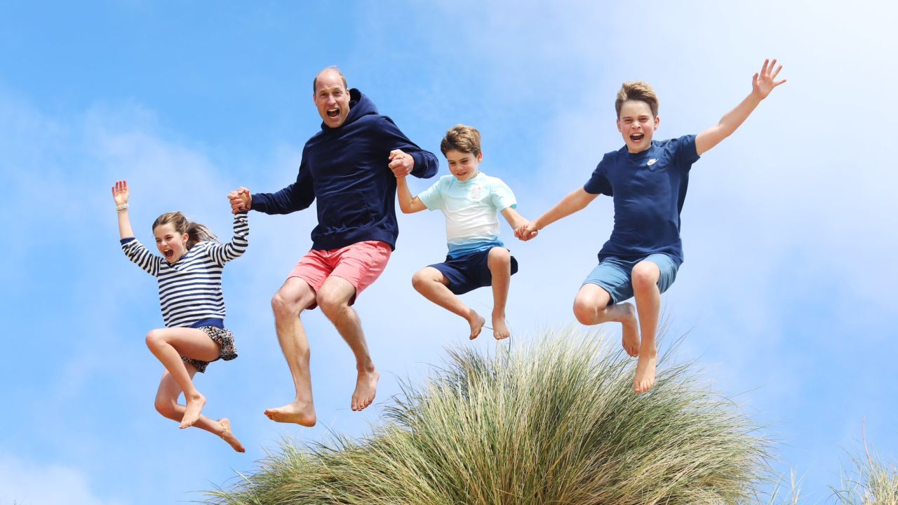 Prince William is pictured jumping off a sand dune with Prince George, Princess Charlotte and Prince Louis.