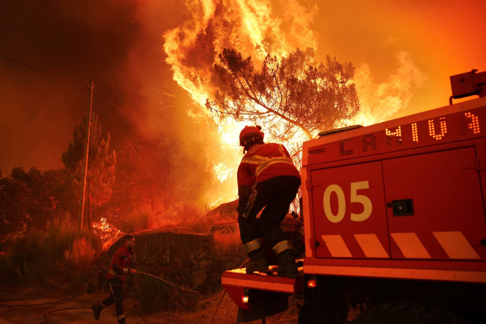 A firefighter helps extinguish a wildfire approaching the Portuguese village of Benvende on Thursday, August 14.