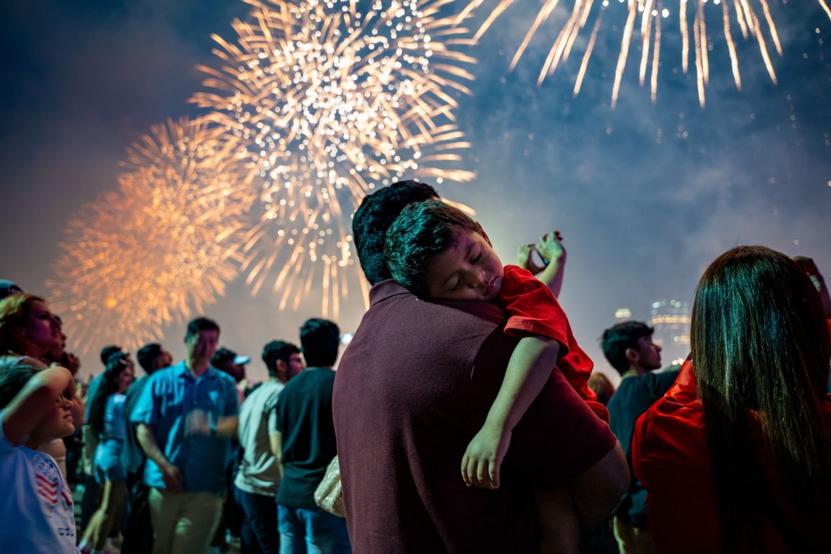 A boy sleeps on his father's shoulder as Fourth of July fireworks light up the sky in New York’s Brooklyn Bridge Park.