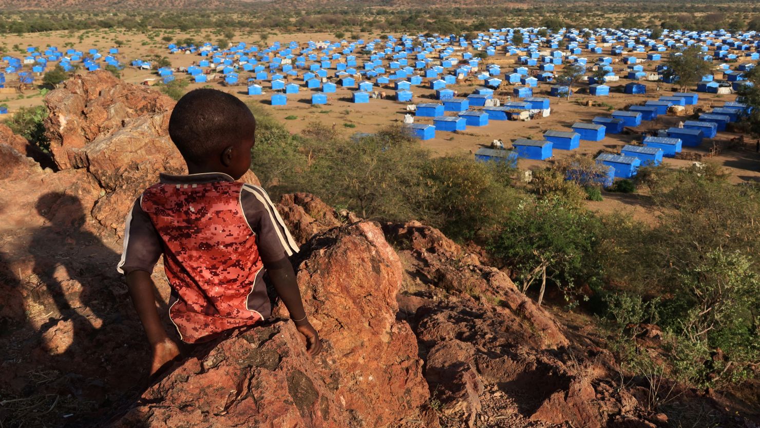 A boy sits atop a hill overlooking a refugee camp near the Chad-Sudan border on November 9, 2023. Hundreds of Masalit families from Sudan's West Darfur state were relocated here months after fleeing to the Chadian border town of Adre, following an ethnically targeted massacre in the city of El Geneina.