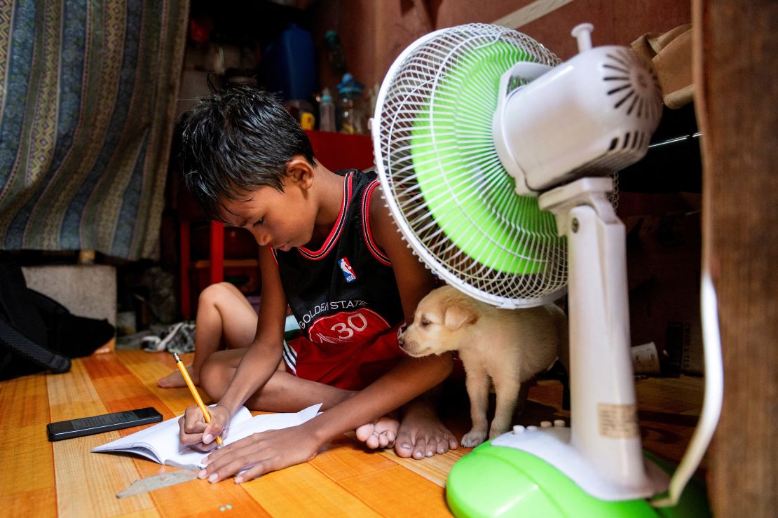 A student doing school work at home in front of a fan following the suspension of in-person classes because of the heat, in Manila, Philippines, April 26, 2024.