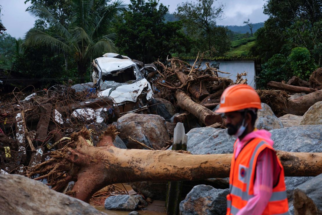 A rescuer walks past uprooted trees, a damaged car and other debris.