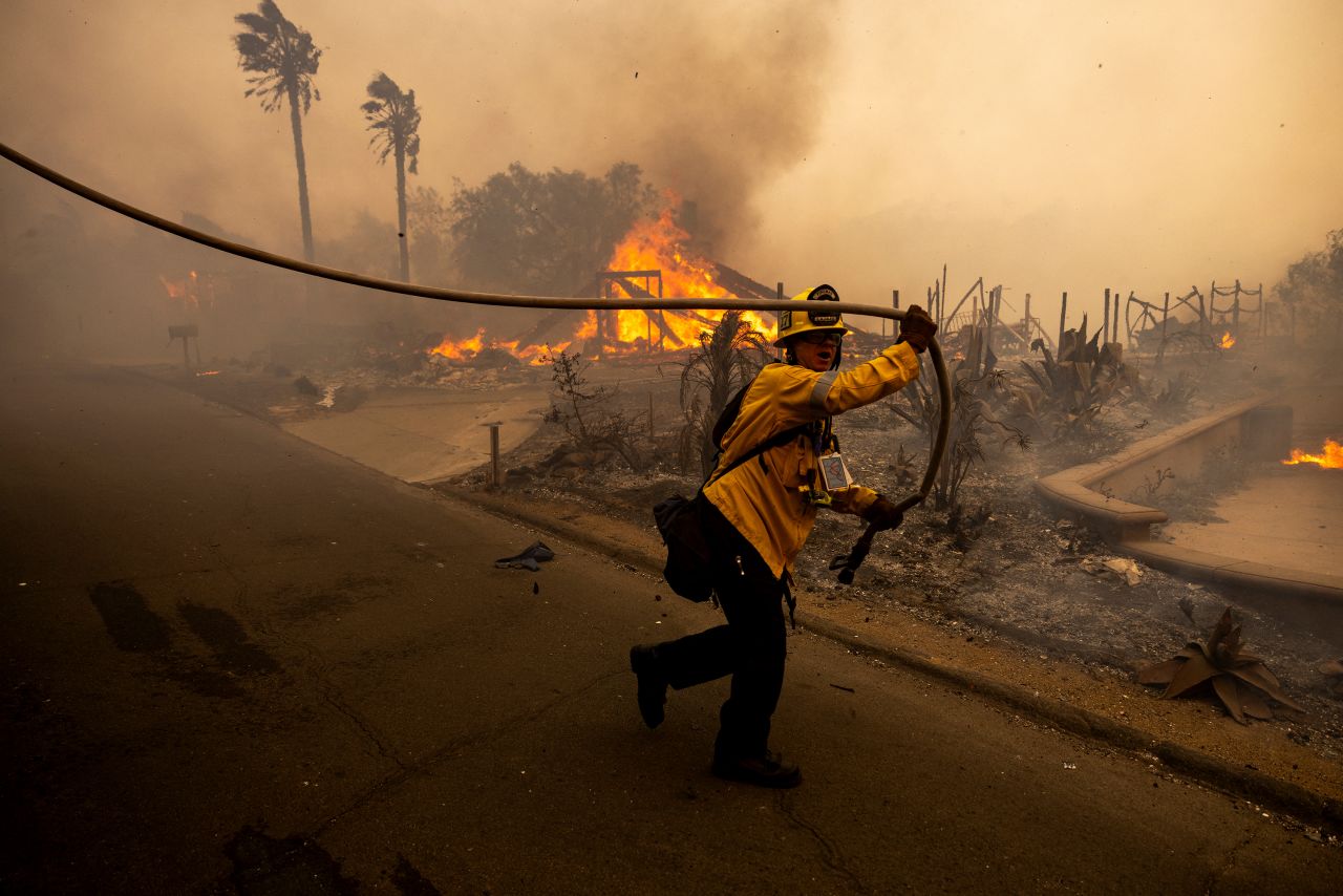 A firefighter pulls a hose in front of a home burned by the Mountain Fire in Camarillo, California, on Wednesday, November 6.