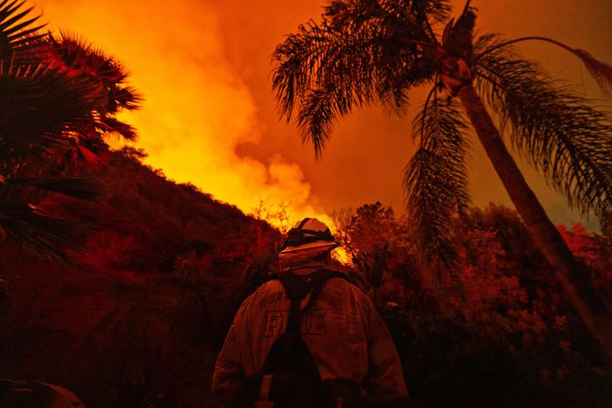 A firefighter stands guard near a home as the Palisades Fire spreads toward the Encino neighborhood of Los Angeles on Saturday, January 11.