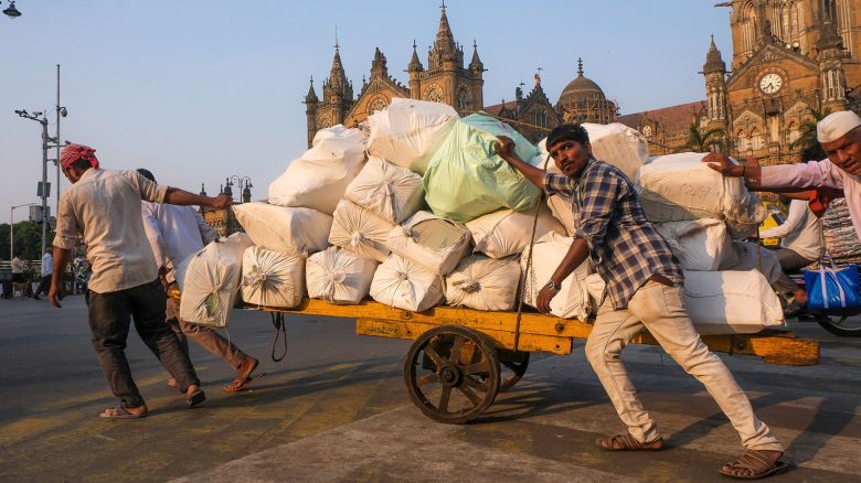 Workers push a cart with packages along a road in front of Victoria Terminus, in Mumbai on April 18, 2024.