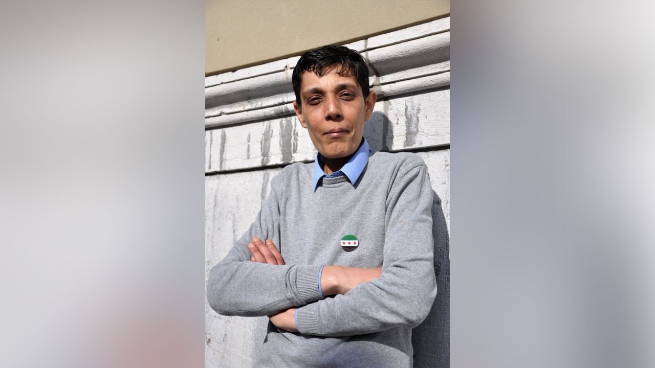 Photo is a headshot of Mazen al-Hamada leaning against a wall with a Free Syria pin.