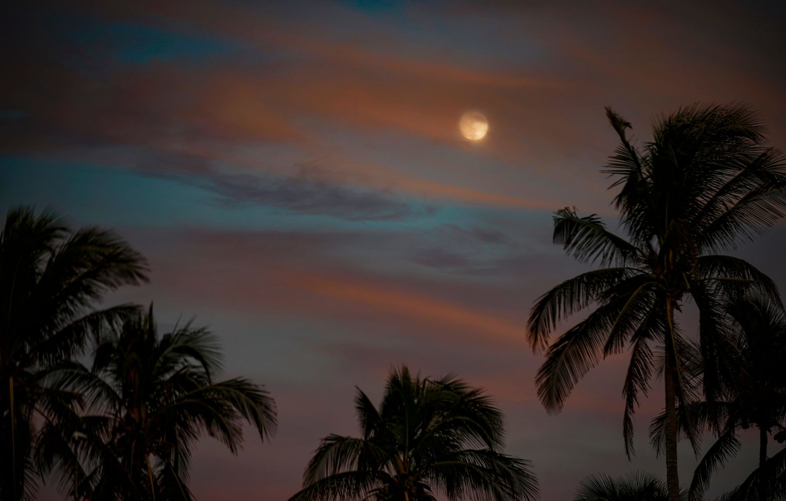 The moon, in its waxing gibbous phase, peaks through cloud cover at the Naples Pier in Naples, Florida, on Tuesday.