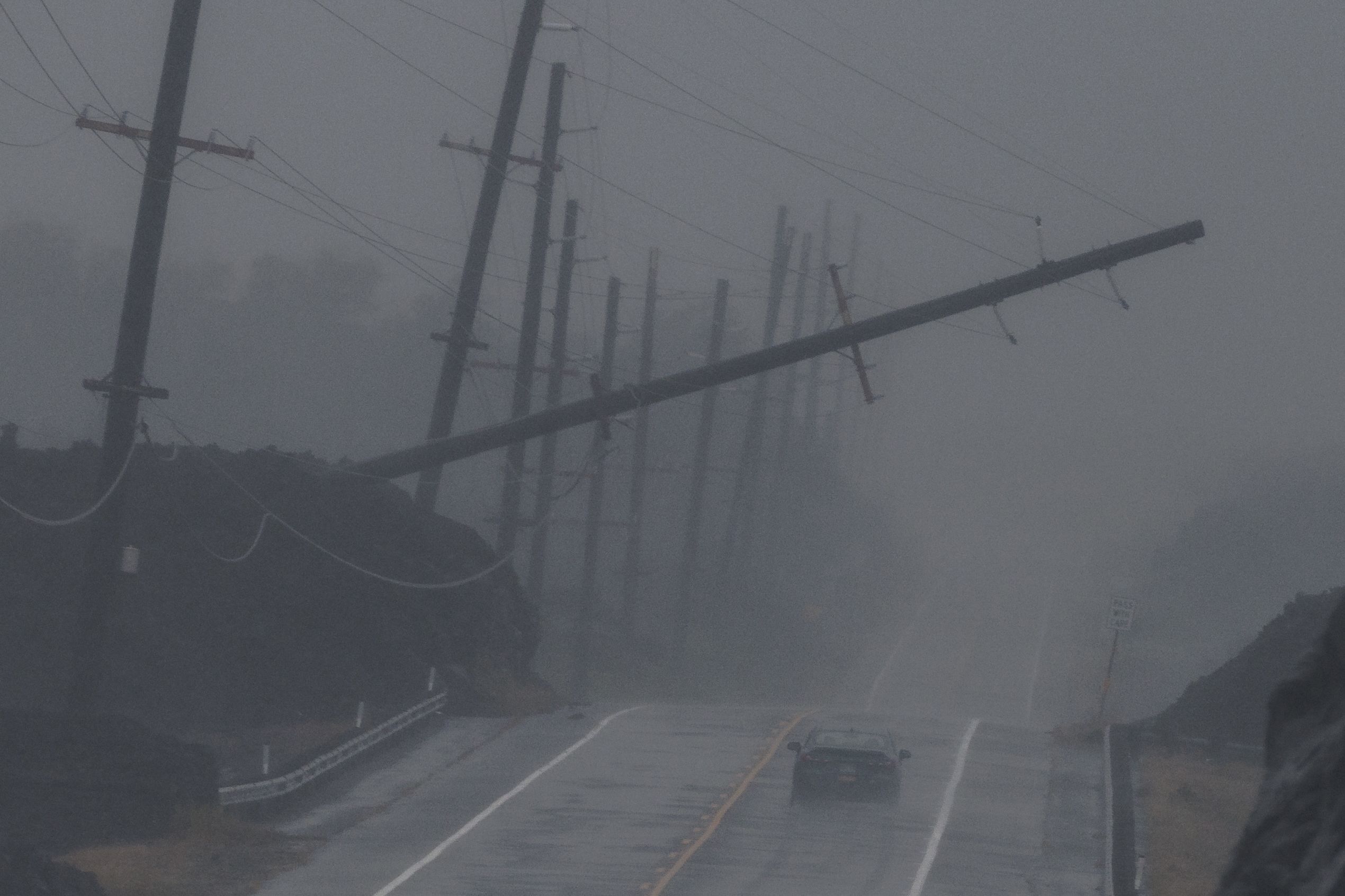 Um veículo se aproxima de um poste de energia caído perto de Ocean View, Havaí, durante o furacão Lala, no sábado, 15 de agosto. <a href="https://www.cnn.com/2026/08/16/weather/tropical-storm-lala-hawaii-damage-climate">A tempestade varreu o sul do estado durante o fim de semana</a>, trazendo chuvas torrenciais que provocaram inundações destrutivas.
