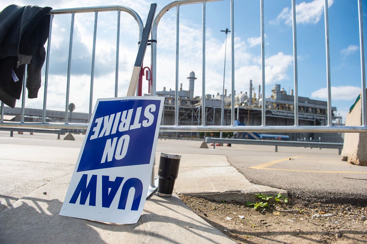 A sign leans against a fence as members of the United Auto Workers (UAW) union walk the picket line in front of Ford Michigan Assembly Plant in Wayne, Michigan, on September 15