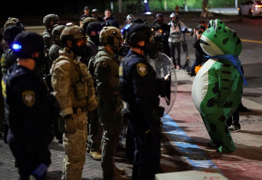 A demonstrator dressed in an inflatable frog costume stands in front of law enforcement officers during a protest outside of the ICE facility in Portland on October 3.