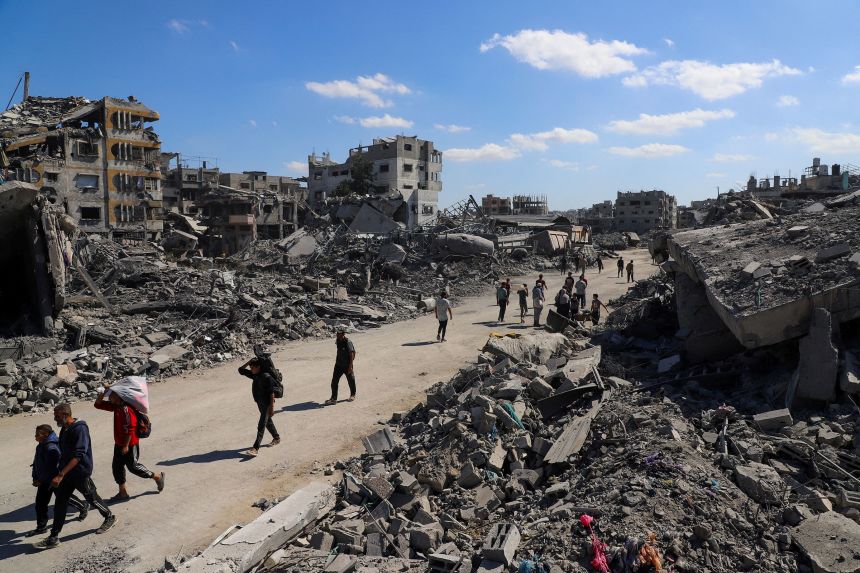 Palestinians walk past the rubble of destroyed buildings in Gaza City, on October 14, 2025.