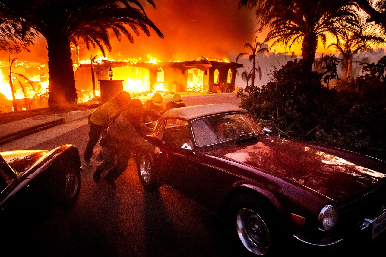 Firefighters and sheriff's deputies push a vintage car away from a burning home in Camarillo on Wednesday.