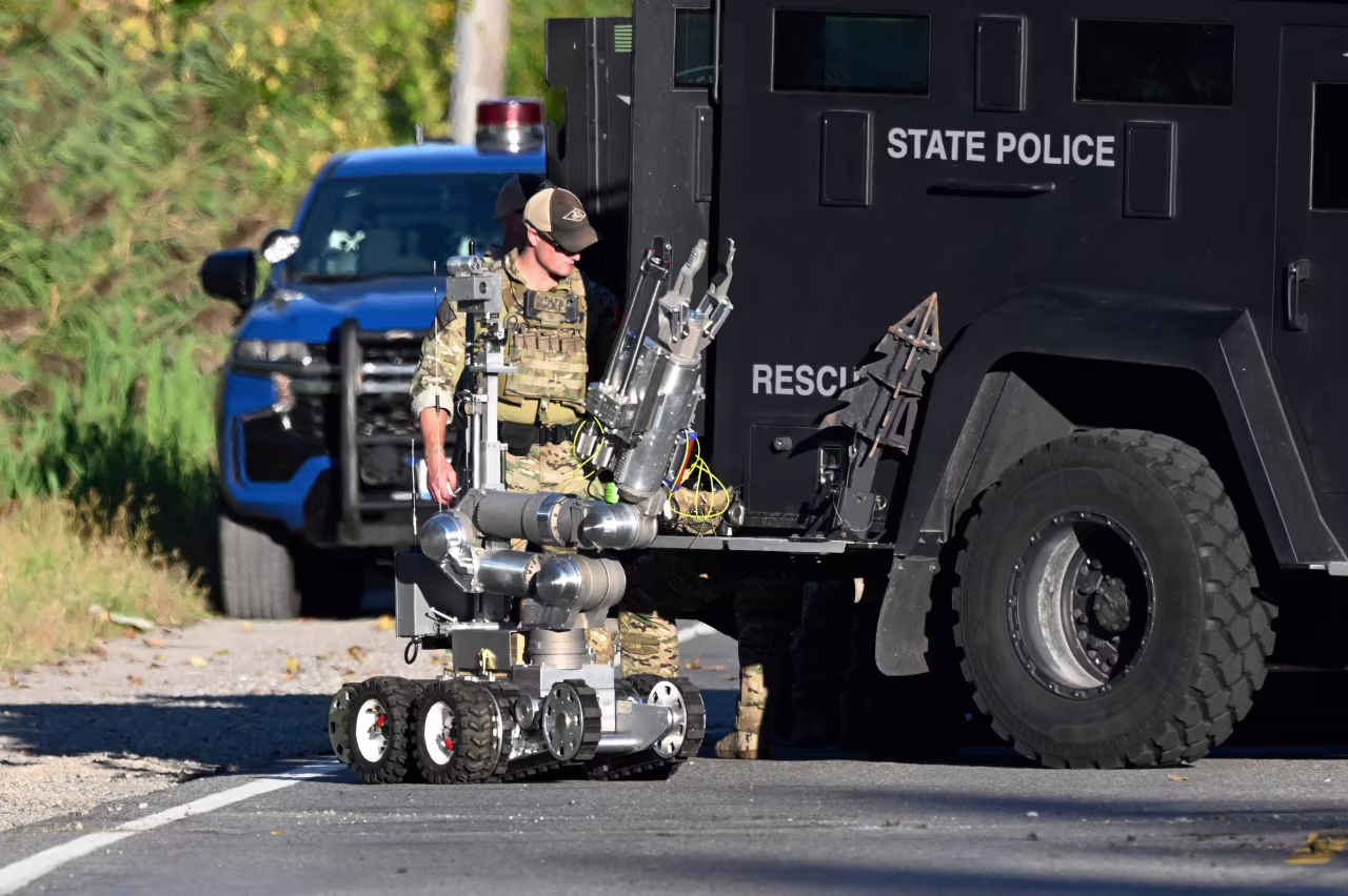 A Michigan State Trooper stands with a robot along East Atherton Road near the home of a suspect allegedly involved in today's shooting.