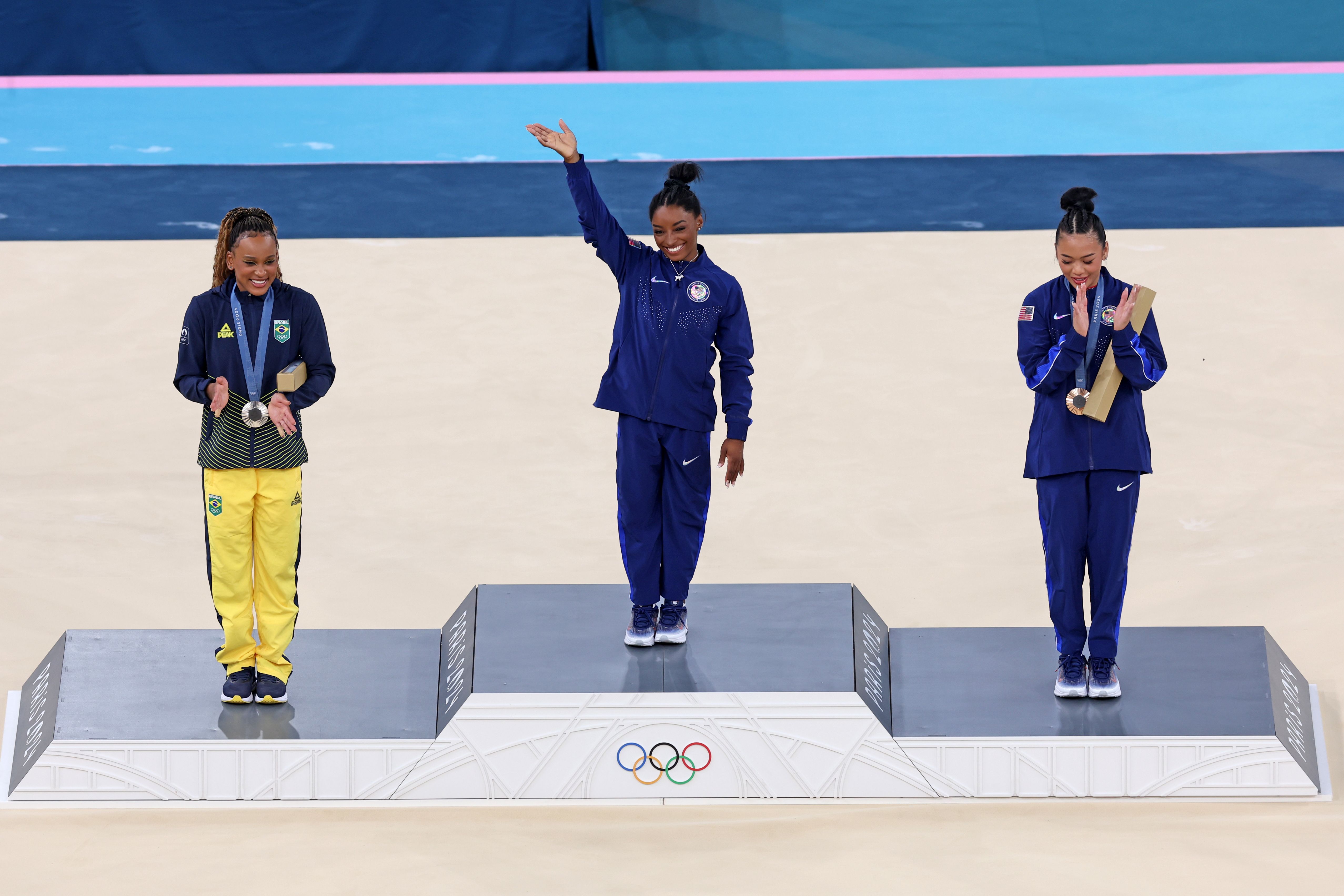 Biles waves on the medal podium Thursday. At left is silver medalist Rebeca Andrade of Brazil. American Suni Lee won bronze.