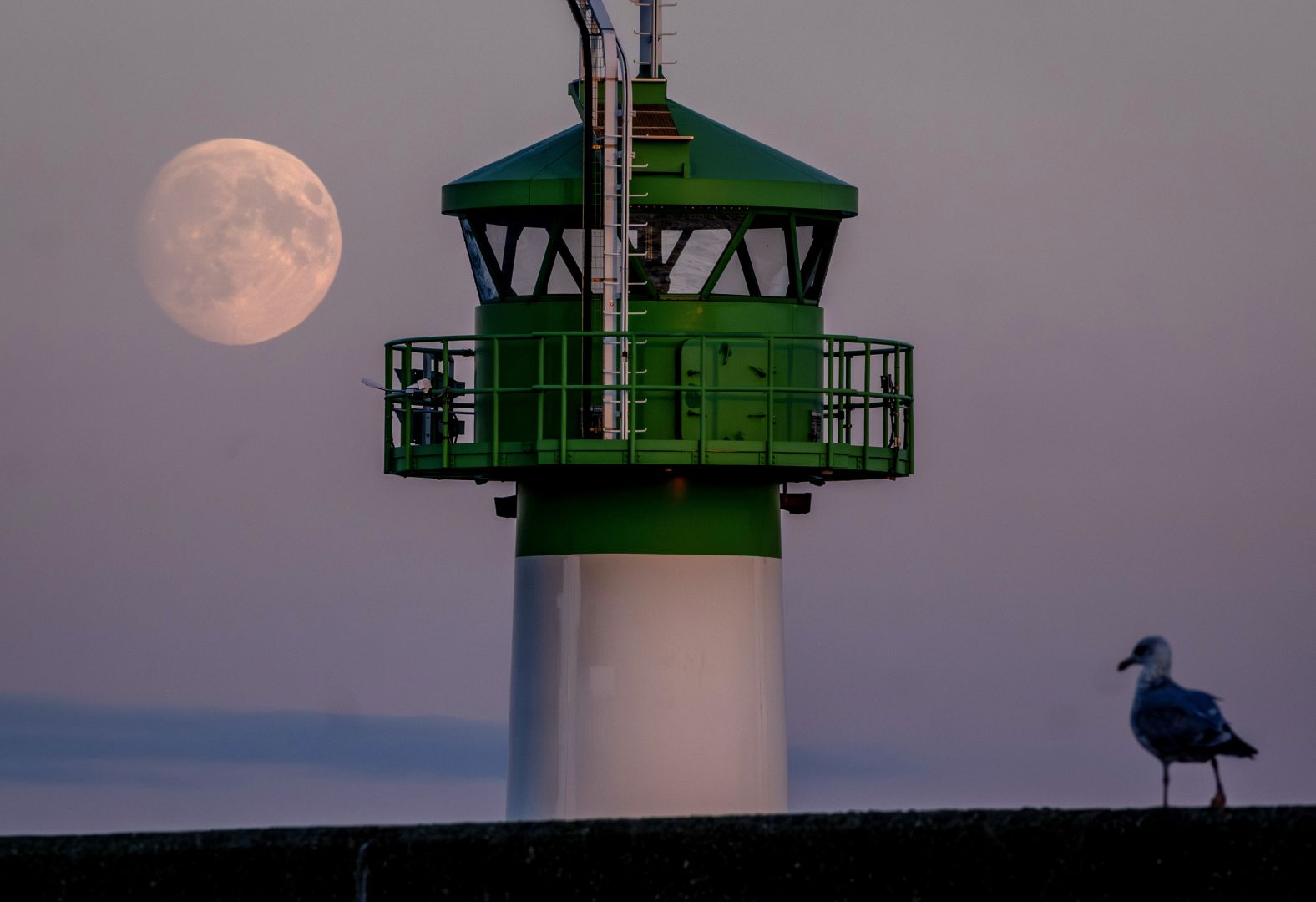 The moon is seen behind a lighthouse at the harbor of Travemünde, Germany, on Tuesday, October 15.