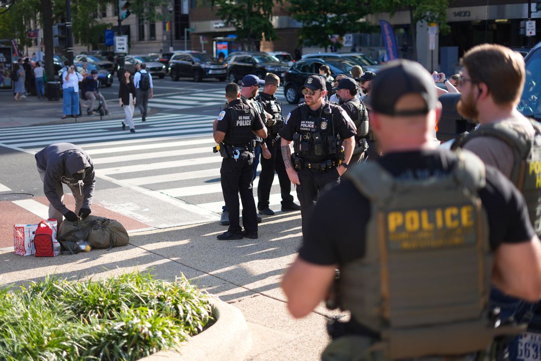 Law enforcement officers for US Park Police and Homeland Security Investigations watch as a homeless individual gathers their belongings after being questioned in Washington, DC's Franklin Park, on Tuesday.