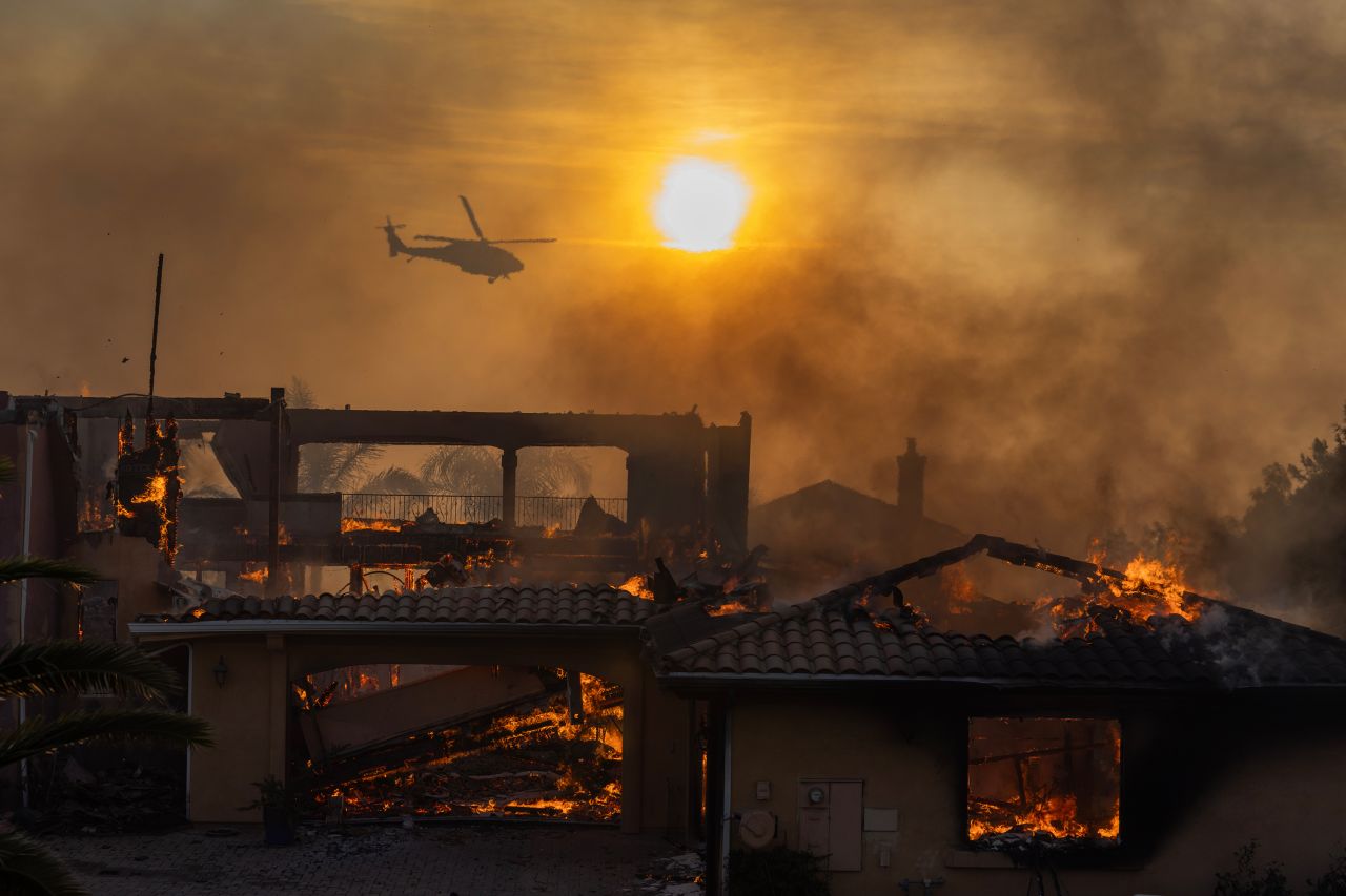 A firefighting helicopter flies near a burning house on Wednesday in Camarillo.