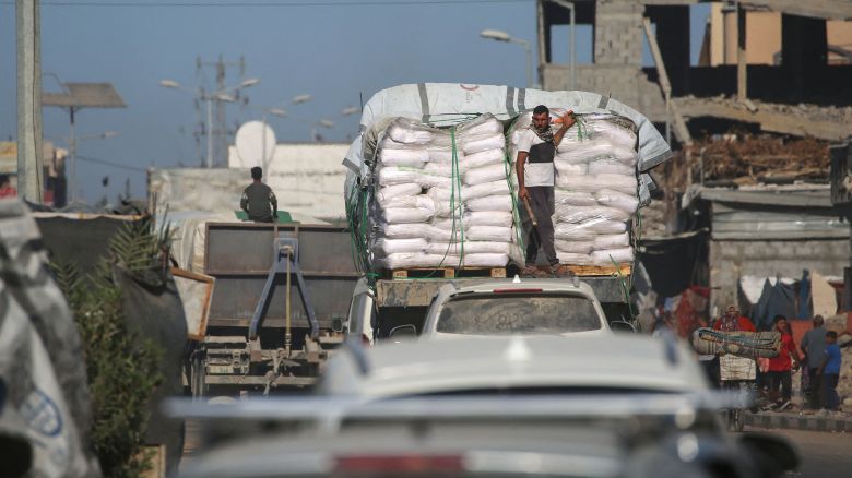 Trucks carrying aid, which entered Gaza through the Karm Abu Salem crossing, drive past displacement tents at the Nuseirat refugee camp in the central Gaza Strip, on October 14, 2025.