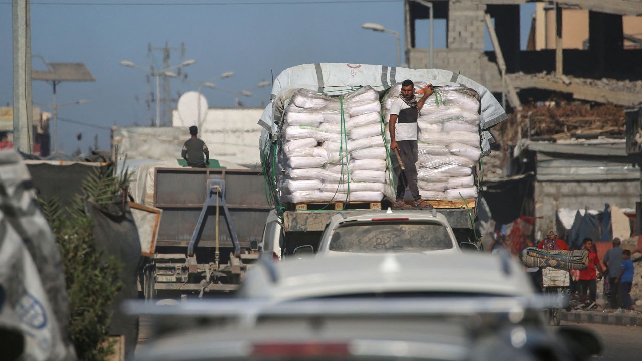 Trucks carrying aid, which entered Gaza through the Karm Abu Salem crossing, drive past displacement tents at the Nuseirat refugee camp in the central Gaza Strip, on October 14, 2025.