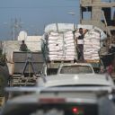 Trucks carrying aid, which entered Gaza through the Karm Abu Salem crossing, drive past displacement tents at the Nuseirat refugee camp in the central Gaza Strip, on October 14, 2025.