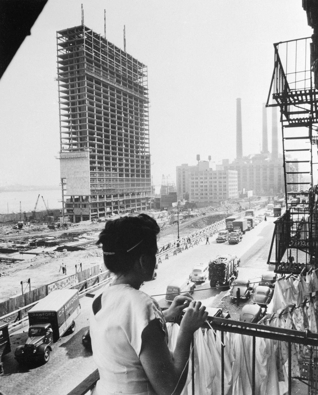 A woman knits as she looks at the steel structure of the United Nations Secretariat Building from a fire escape in New York.