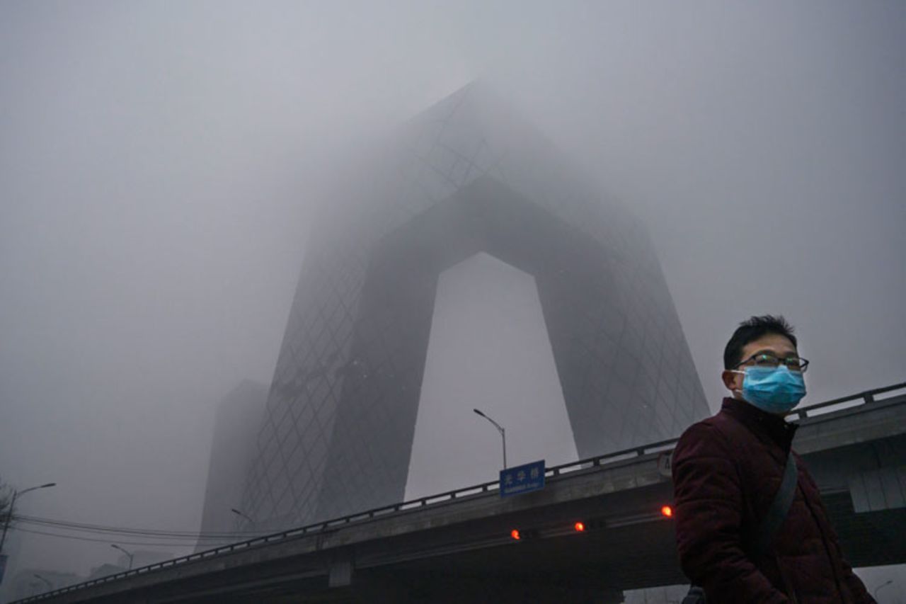 A Chinese man wears a protective mask as he passes near the CCTV building in fog and pollution during rush hour in the central business district on February 13, in Beijing, China. 