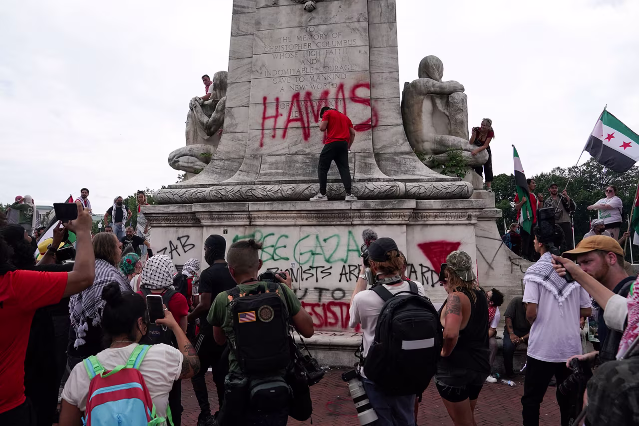 A demonstrator sprays graffiti, including the word "Hamas," on the Christopher Columbus Memorial Fountain at Union Station.
