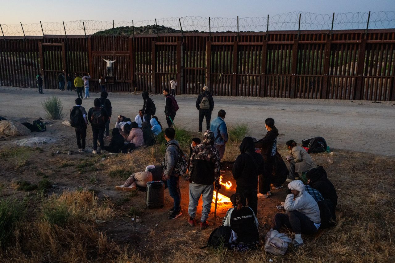 Migrants sit by a makeshift fire to warm up after crossing into the US from Mexico on June 14, in Jacumba Hot Springs, California. The Trump campaign is using Minnesota Gov. Tim Walz's immigration policies to attack Vice President Kamala Harris, who named Walz her running mate.